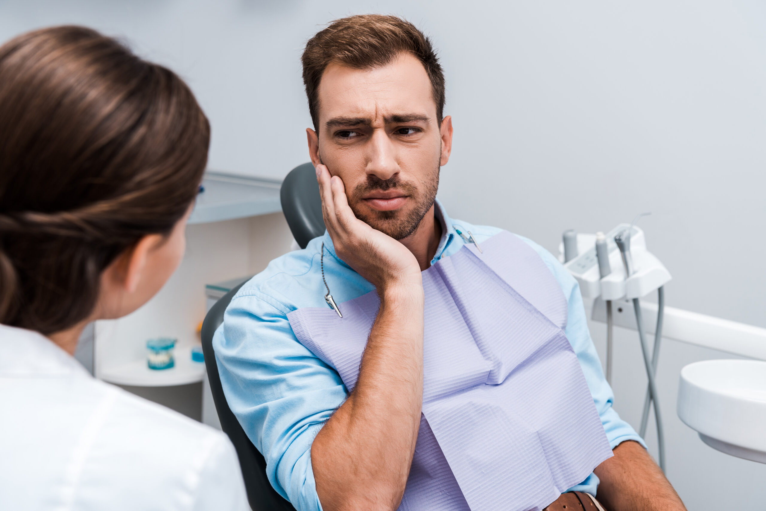 Patient touching cheek in pain from a toothache, a common dental emergency sign